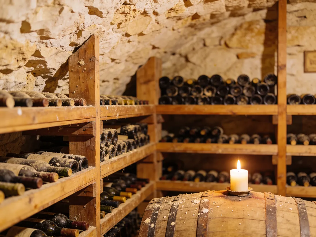 La cantina scavata nel tufo, bottiglie sugli scaffali di legno e una candela sulla botte